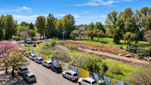 Cantiere del parcheggio P2 di Acilia Sud, lungo via Bepi Romagnoni a Roma, con l'area interessata dai lavori e le alberature circostanti.