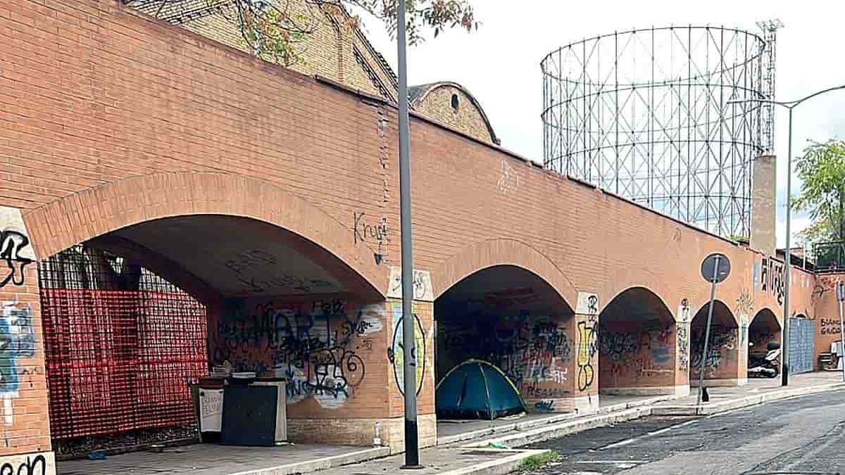 Porticato di via Avogadro vicino all'ex Mira Lanza, nel quartiere Marconi a Roma, con una tenda blu sotto gli archi e il Gazometro sullo sfondo.