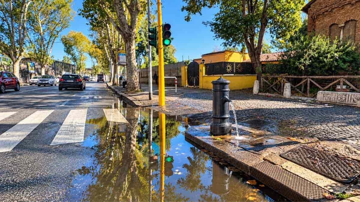 Magliana, ristagno d'acqua vicino alle strisce pedonali di via della Magliana, accanto a una fontanella pubblica e a un semaforo.