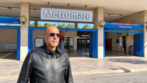 Giuseppe Conforzi davanti alla stazione Cristoforo Colombo della Metromare a Ostia, con l'ingresso ferroviario sullo sfondo.