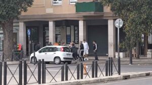 Ostia, gruppo di persone coinvolte in uno scontro sul marciapiede nei pressi della stazione Lido Centro della Metromare, con volti e targa oscurati.