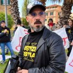 Manifestante con megafono e maglia di Giustizia X Ostia, circondato da persone e striscioni durante una protesta a Ostia.