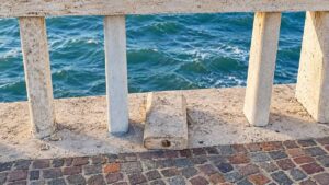 Ostia, elemento di marmo fuori sede sulla balaustra del Pontile, appoggiato sul basamento del parapetto con il mare sullo sfondo.