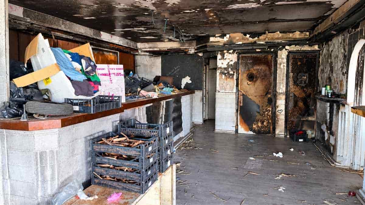 Ostia, interno dell'ex Algida con soffitto annerito, pareti deteriorate, materiali accatastati e rifiuti abbandonati.