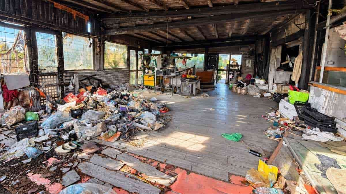 Interno dell'ex Algida di Ostia con cumuli di rifiuti, materiali abbandonati, finestre danneggiate e soffitto annerito.