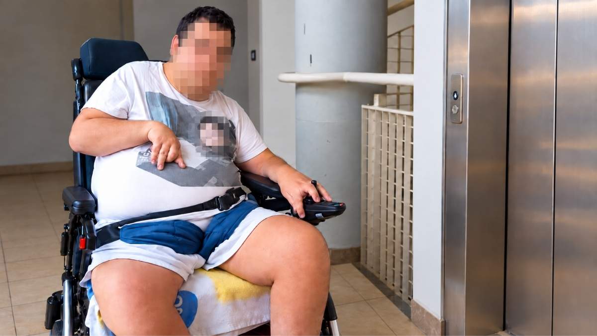 Ragazzo in carrozzina davanti all’ascensore di una palazzina Ater a Corviale, Roma, con il volto oscurato per tutelarne la privacy.