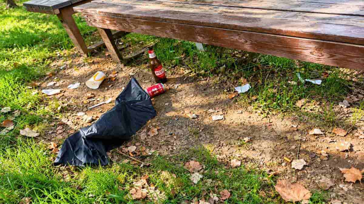 Roma, bottiglia di vetro, lattina, bicchiere e sacchetto nero abbandonati sotto un tavolo da picnic nel Parco Tevere Magliana.