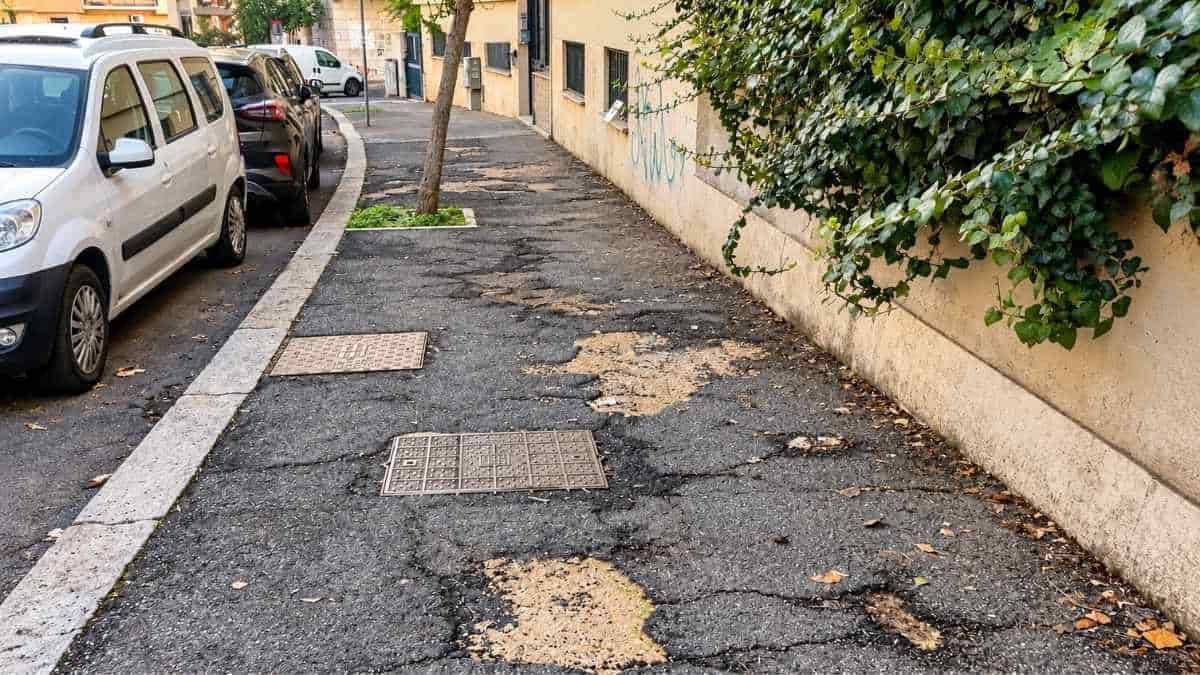 Roma, marciapiede dissestato con crepe e asfalto deteriorato a Tor Marancia, nell'area vicina agli istituti scolastici.