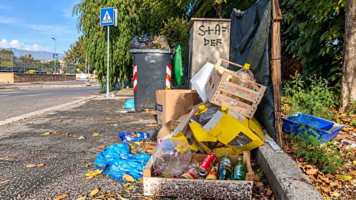 Roma, scatoloni, cassette, bottiglie di vetro e plastica abbandonati sul marciapiede di via Don Tonino Bello, vicino a un cassonetto.